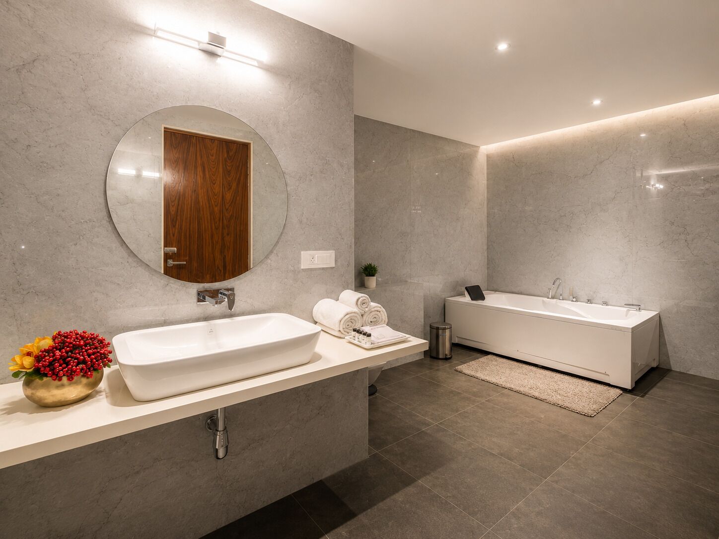 Un bany modern amb un lavabo gran, un mirall rodó, una porta de fusta, una banyera i una petita planta en test.