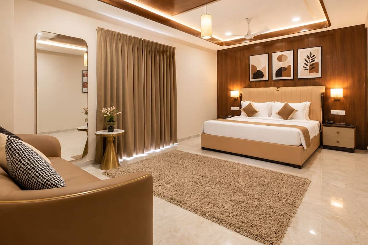 A modern hotel room with a large bed, a sofa, a small round table, and a mirror.