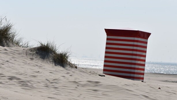 A beach with sand dunes and a striped beach umbrella. - Wellmann Modern Retreat (Borkum)