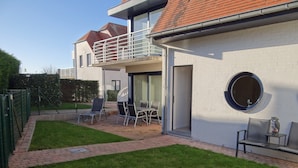 Una casa moderna con un patio que tiene una mesa, sillas, un pequeño jardín y un ventanal redondo.