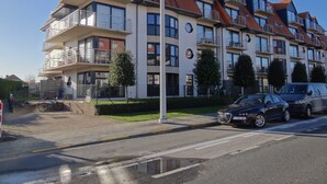 Un edificio residencial de varios pisos con balcones, un estacionamiento y cielo despejado.