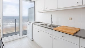 A modern kitchen with white cabinets, a stainless steel sink, and a wooden cutting board. - Cozy 1-bedroom Apartment With Sea View (Middelkerke)