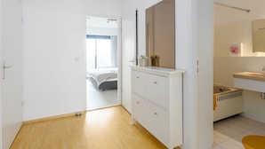 A modern bedroom with a large bed, a wardrobe with drawers, a mirror, and a bathroom with a sink and toilet. - Cozy 1-bedroom Apartment With Sea View (Middelkerke)