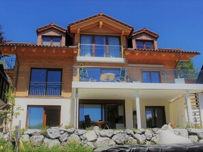 Et toetagers hus med balkon, store vinduer og en stenvæg foran.