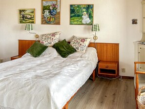A bedroom with a wooden bed, green and floral pillows, a white quilt, and two wall-mounted lamps. - 6 Person Holiday Home in Skummeslovsstrand (Skummesloevsstrand)
