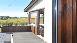 A wooden deck with a view of a grassy field and a building in the background. - 6 Person Holiday Home in Skummeslovsstrand (Skummesloevsstrand)