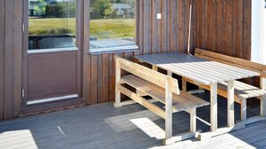 A wooden deck with a bench and a table, a door, and a view of a grassy area through a window. - 6 Person Holiday Home in Skummeslovsstrand (Skummesloevsstrand)