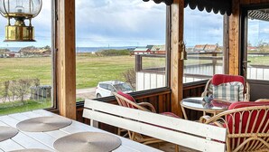 A wooden deck with a white table and wicker chairs, overlooking a grassy field and a distant red barn. - 6 Person Holiday Home in Skummeslovsstrand (Skummesloevsstrand)