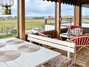 A wooden deck with a white table and wicker chairs, overlooking a grassy field and a distant red barn. - 6 Person Holiday Home in Skummeslovsstrand (Skummesloevsstrand)