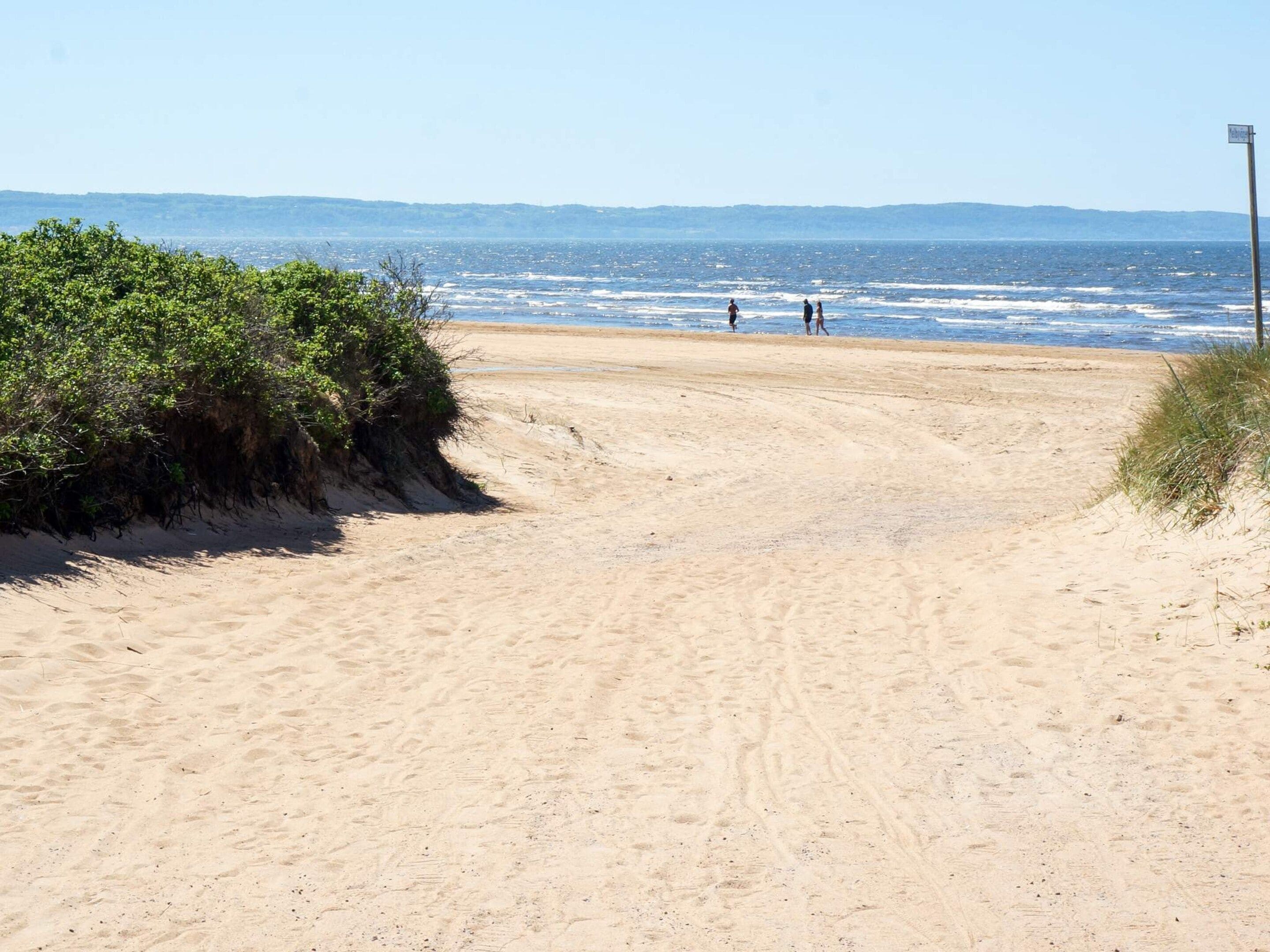 Een zandstrand met voetafdrukken die naar het water leiden, een heldere lucht en heuvels in de verte.