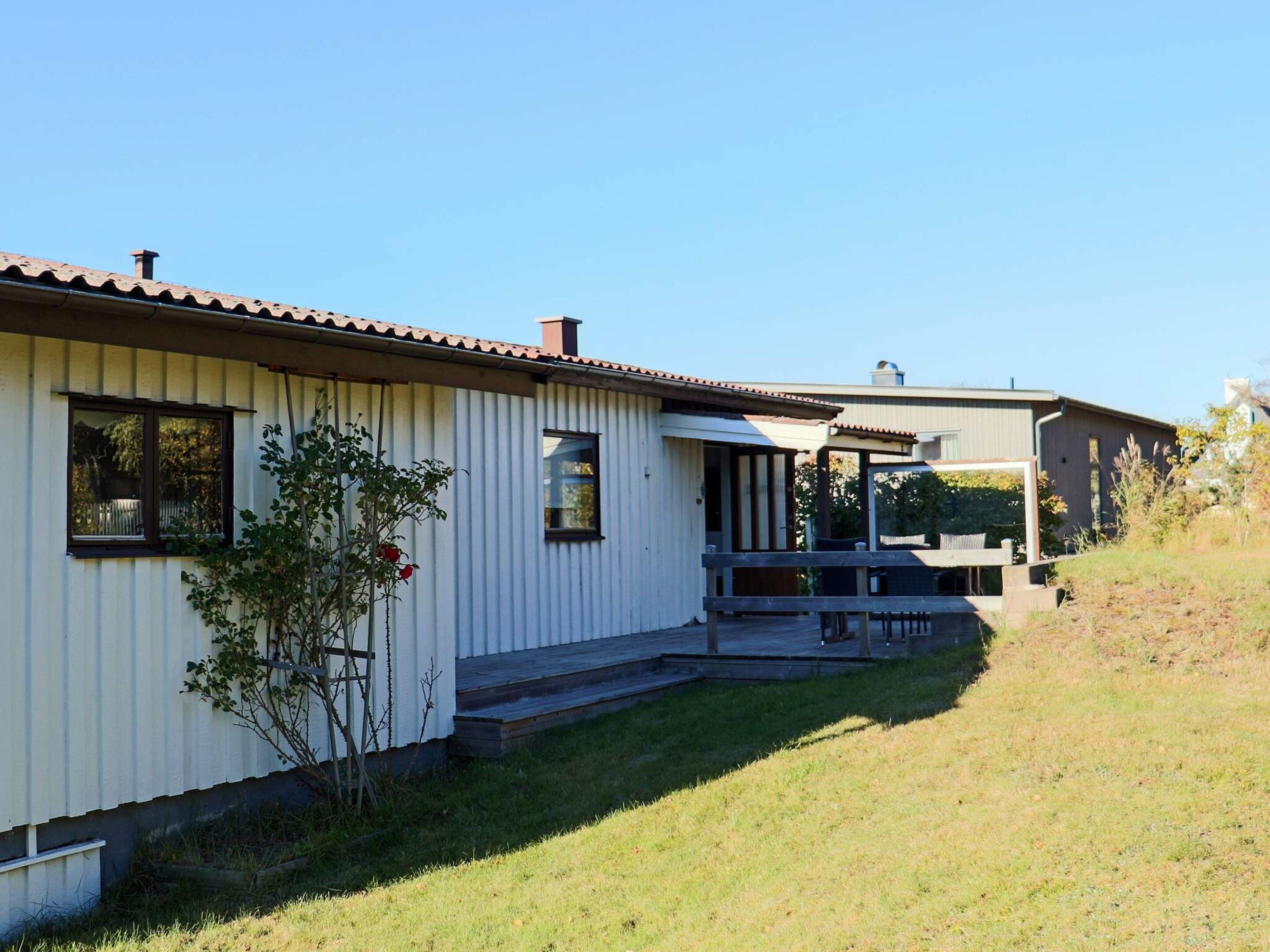 A single-story building with a flat roof, a porch, and a small garden area.