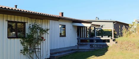 A single-story building with a flat roof, a porch, and a small garden area.