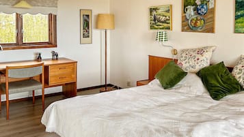 A bedroom with a wooden desk, a bed with green pillows, and wall art.