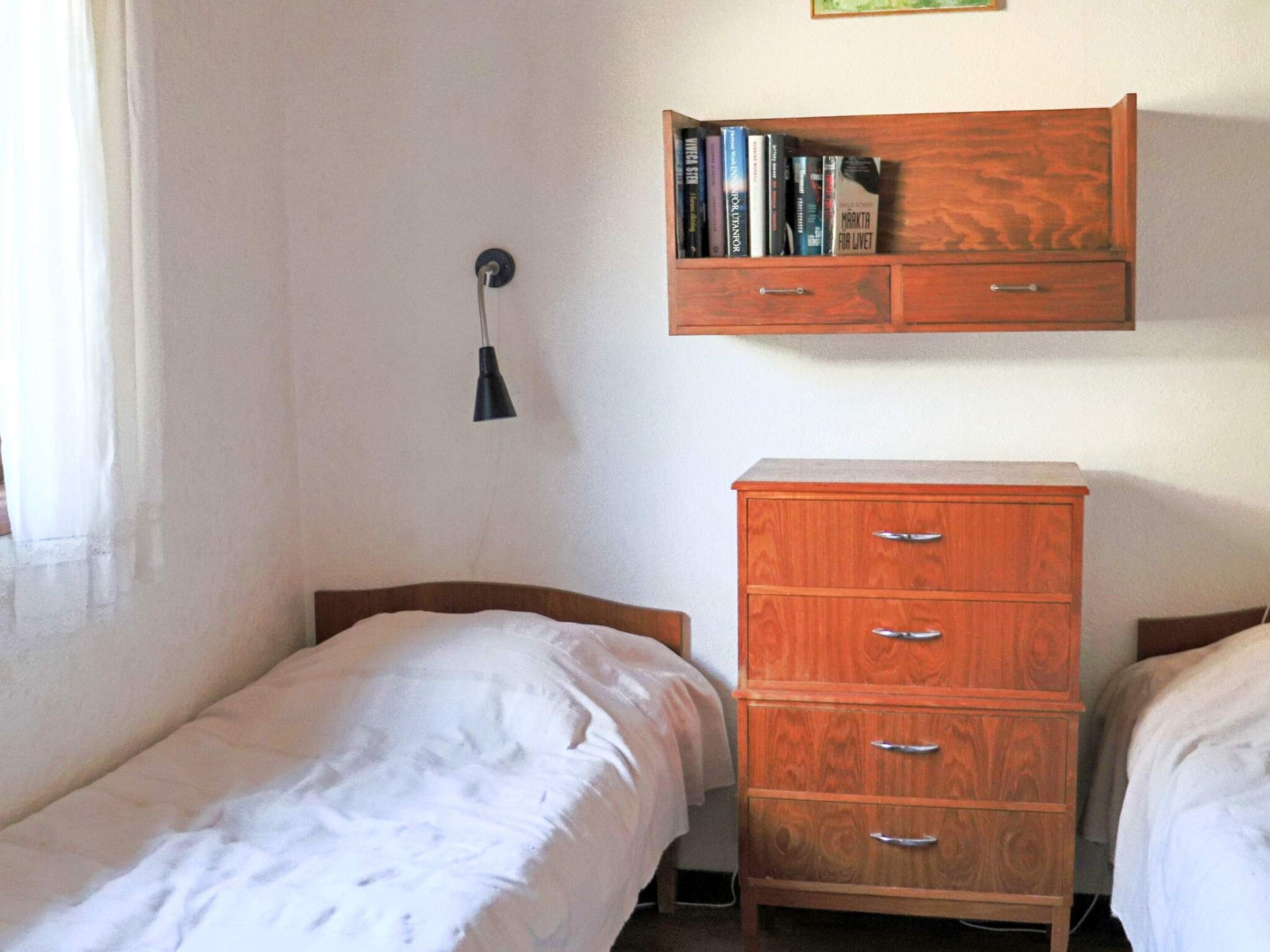 Une chambre avec deux lits simples, une commode en bois et une étagère murale remplie de livres.