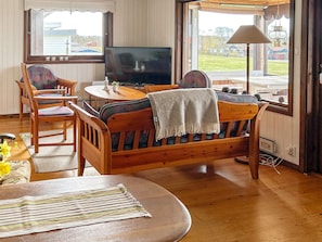 A cozy living room with a wooden sofa, chairs, a television, and a view of the outdoors through large windows. - 6 Person Holiday Home in Skummeslovsstrand (Skummesloevsstrand)