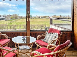 Una habitación con muebles de mimbre y una mesa de vidrio, con vista a un área verde y una masa de agua.