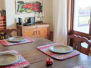 A dining table with placemats and plates, a coffee pot, and a painting on the wall.
