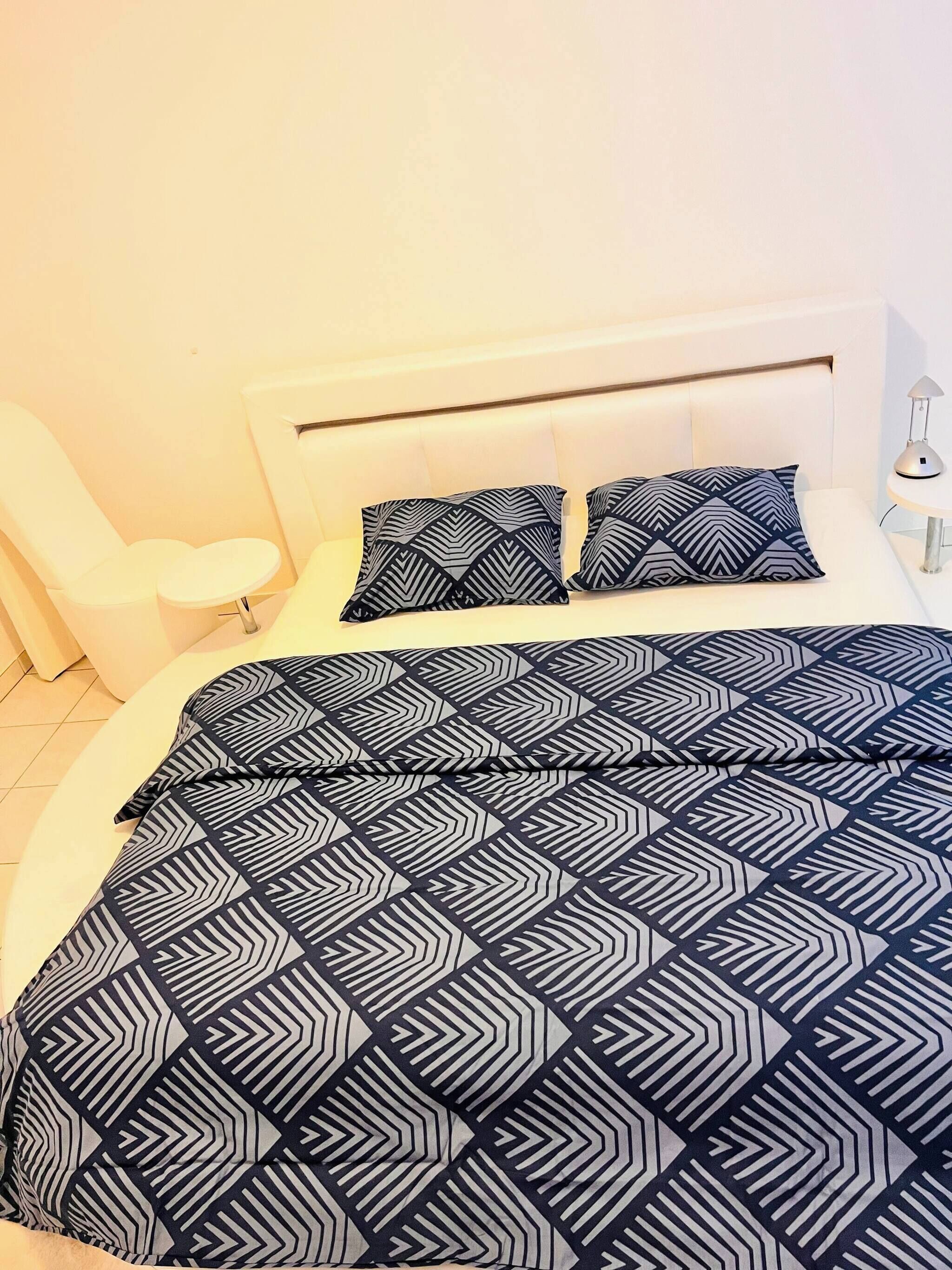 Ein Schlafzimmer mit einem Bett, zwei Kissen, einer Nachttischlampe und einem Sessel.