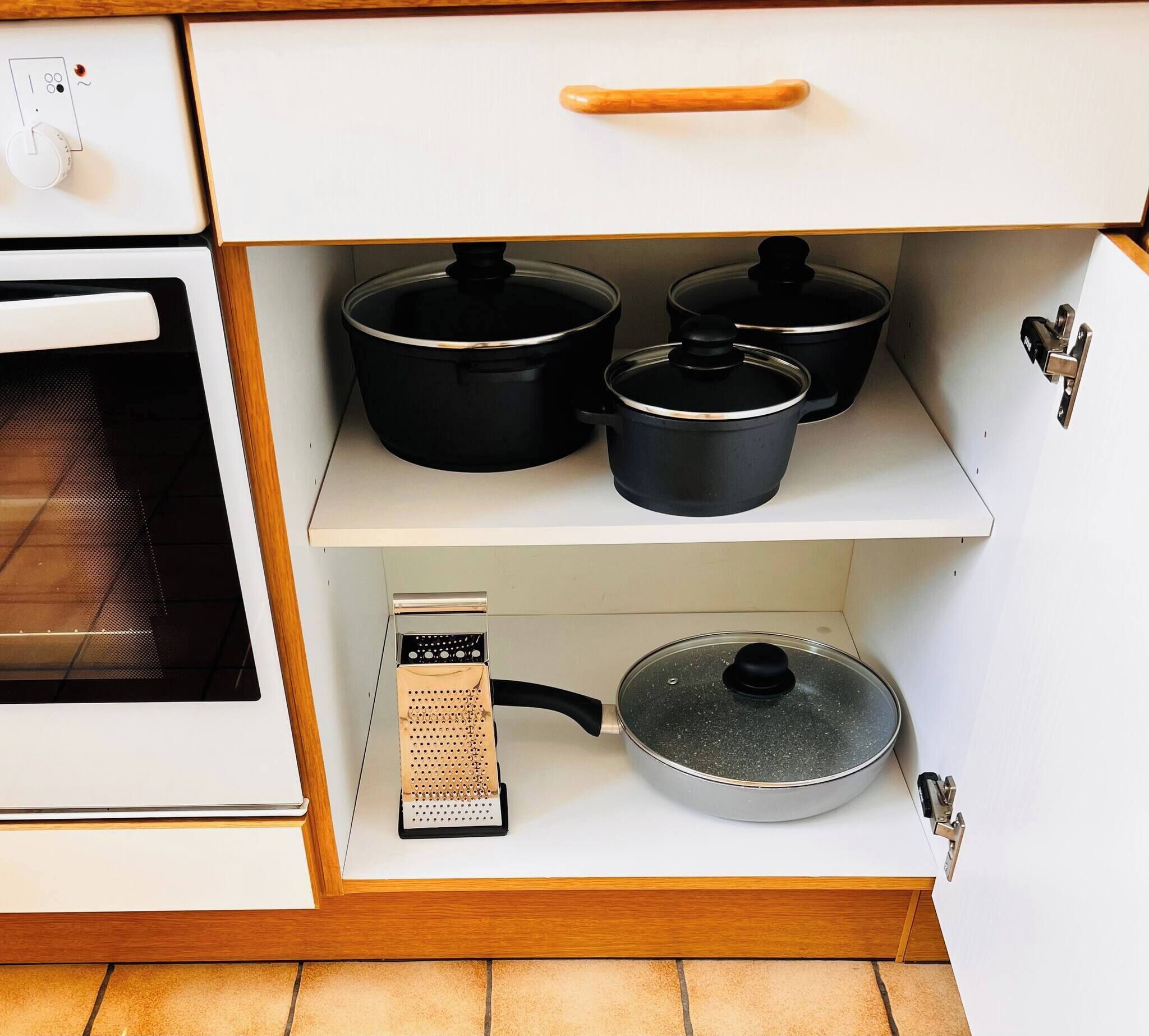 A kitchen with a stove, oven, and three black pots on a shelf.