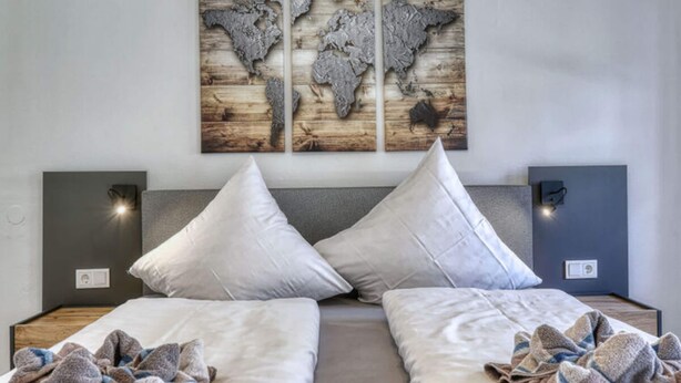 A double bed with two pillows, a world map artwork above, and bedside lamps on either side. - Haus Leutner Bodenmais (Bodenmais)