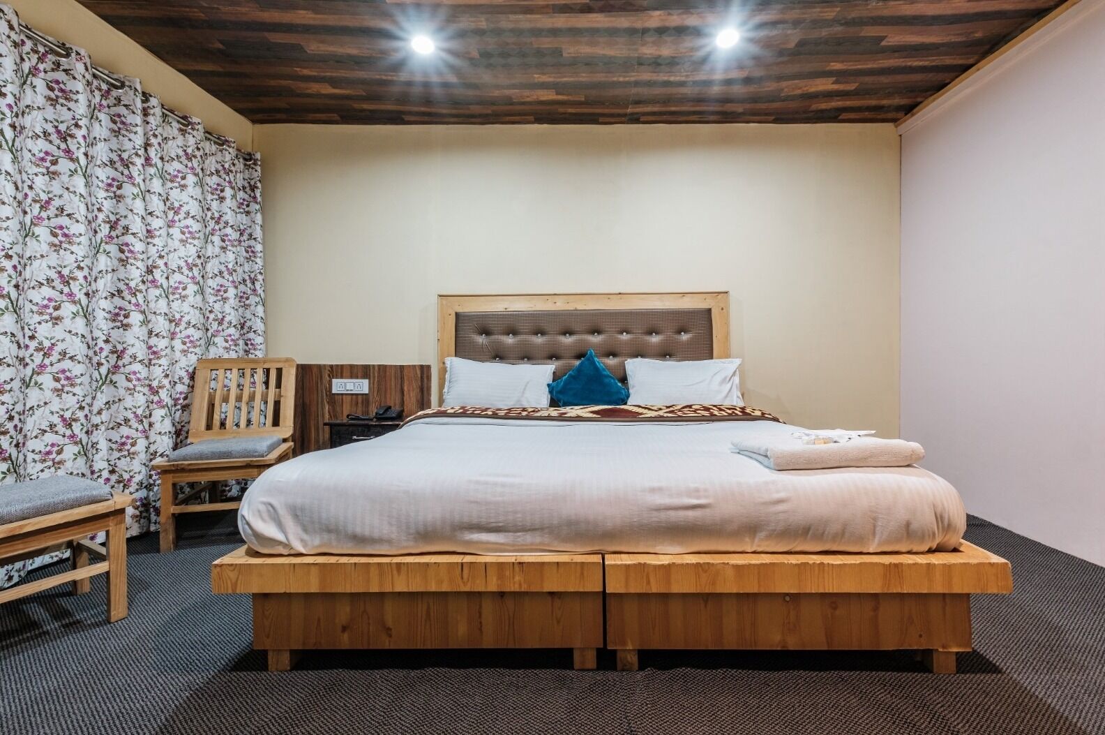 A bedroom with a wooden bed, a chair, a nightstand, and a floral curtain.