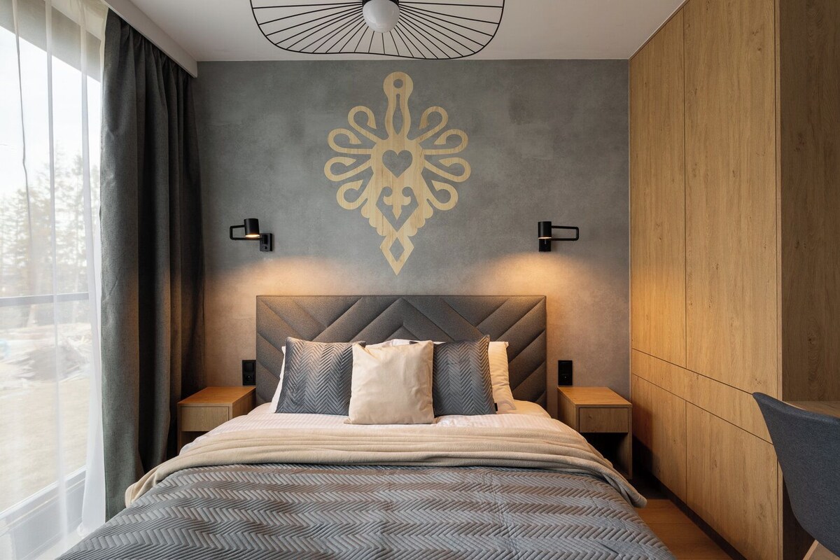 A modern bedroom with a large bed, a geometric wall design, and two bedside lamps.