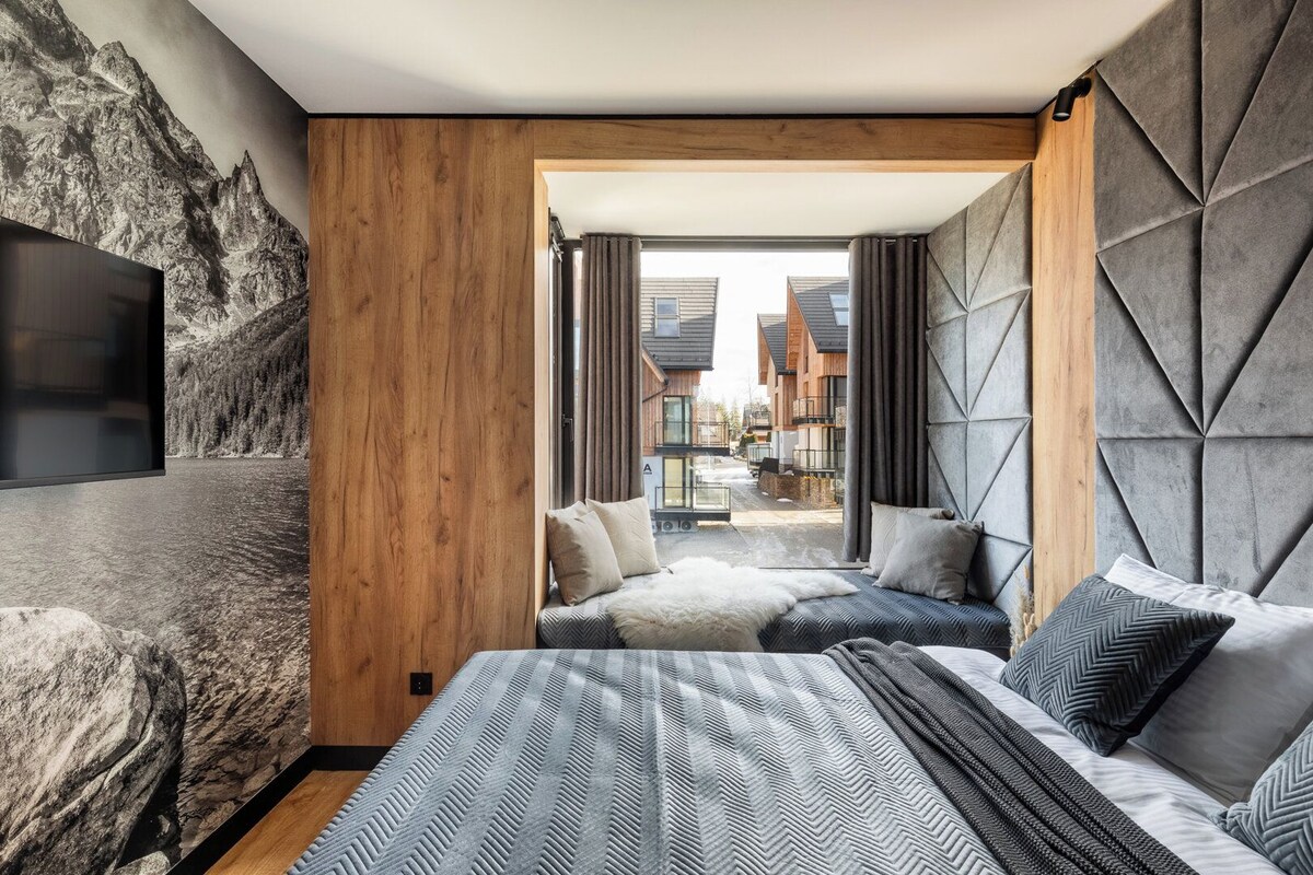 A modern bedroom with a large bed, a TV, and a view of a mountain landscape.