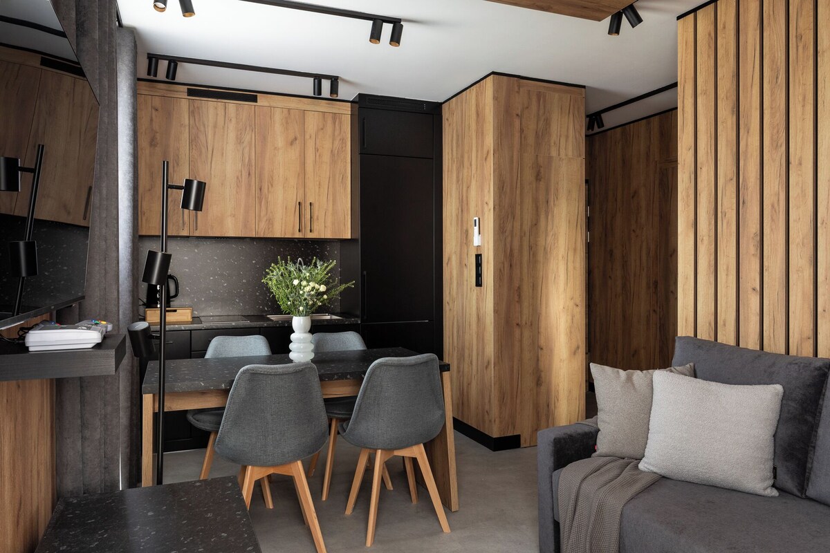 A modern kitchen with wooden cabinets, a dining area with two chairs, and a grey sofa.
