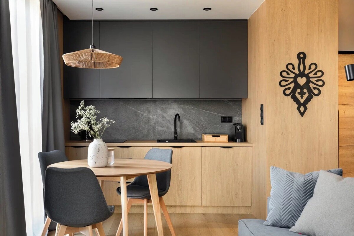 A modern kitchen with dark cabinets, a round wooden table, and a hanging light fixture.