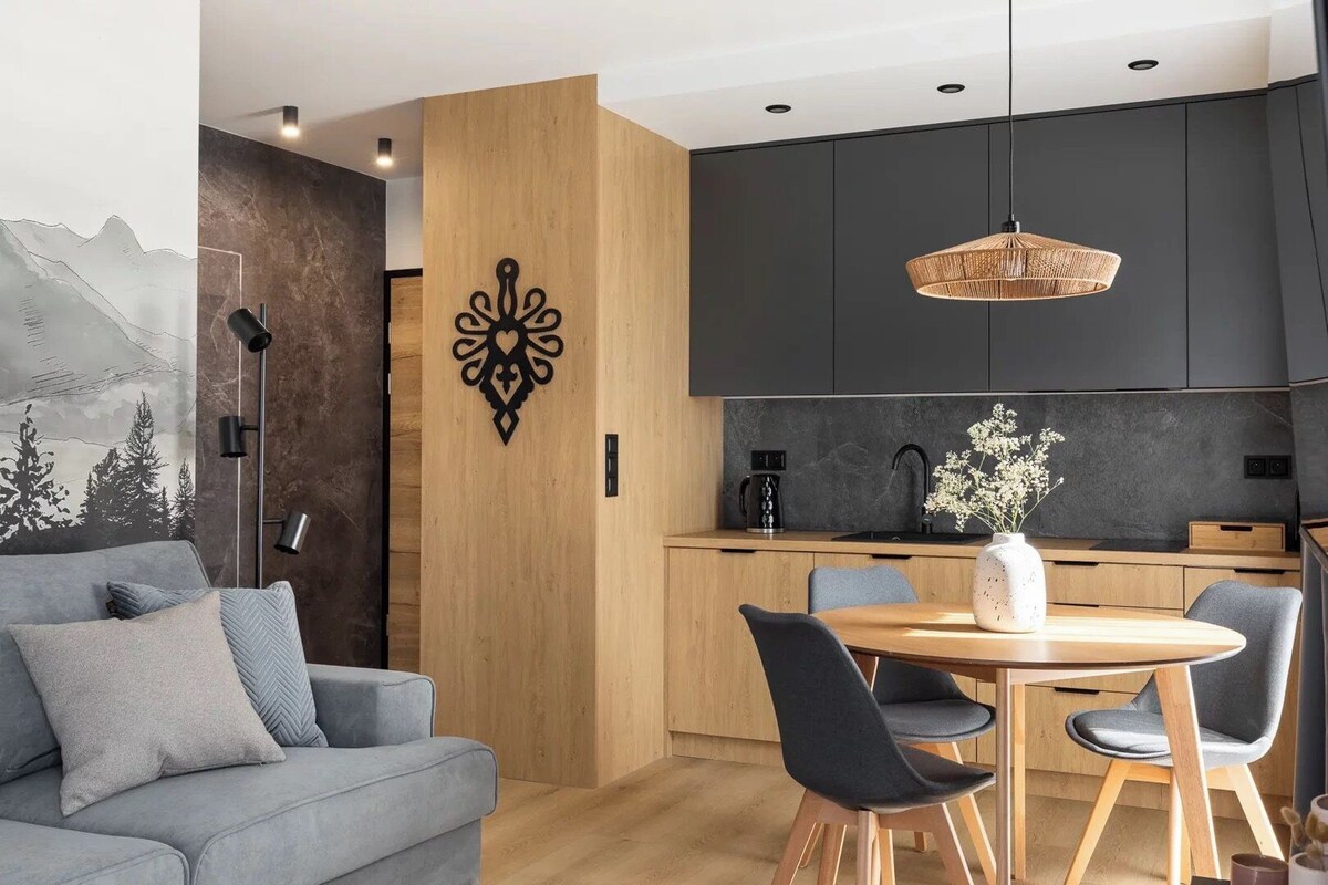 A modern kitchen with dark cabinets, a round wooden table, and a hanging light fixture.