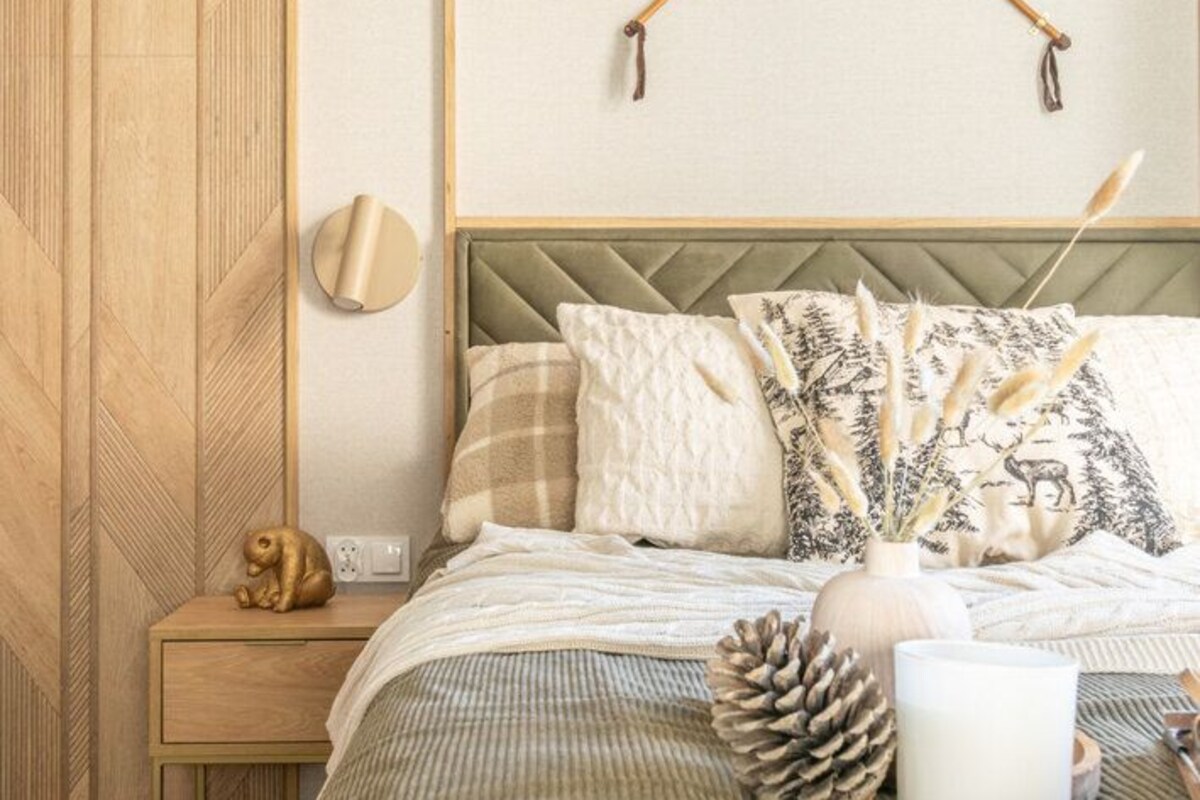 A bedroom with a bed, a nightstand, a wall-mounted lamp, and a decorative wall piece.