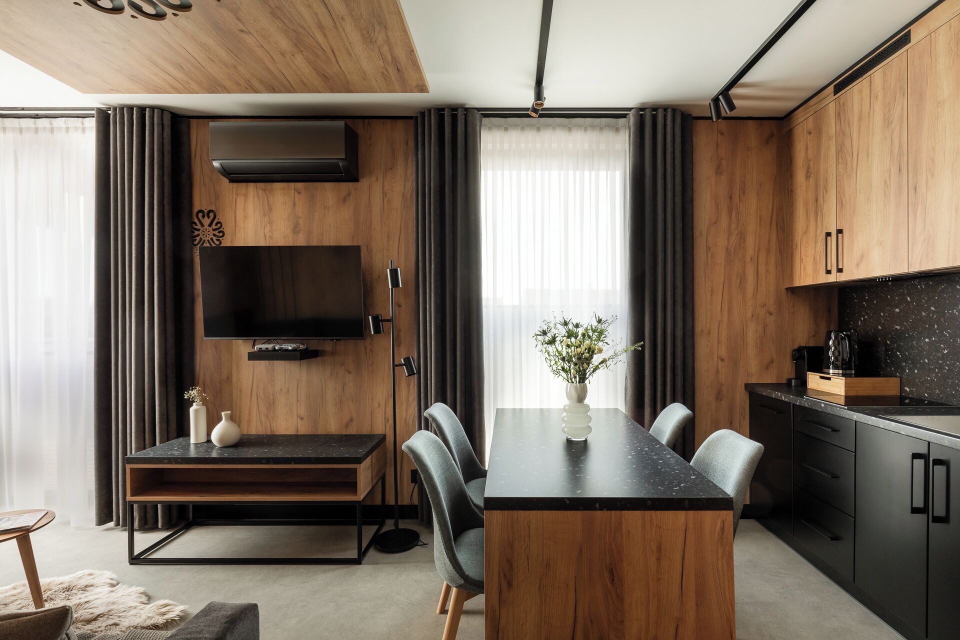 A modern kitchen with wooden cabinets, a black countertop, and a dining area with a wooden table and chairs.