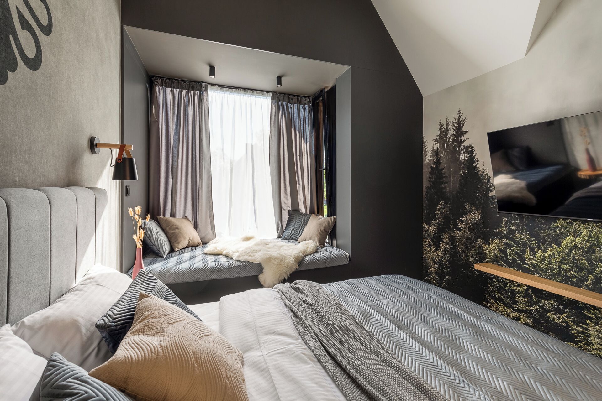 Een slaapkamer met een groot bed, een raam met gordijnen, een bevestigde televisie en een wandplank.