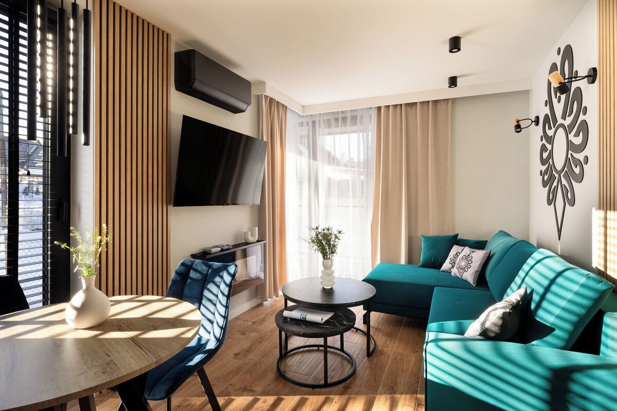 A modern living room with a sofa, a TV, a coffee table, and a dining area with a chair and table.
