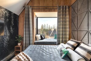 A bedroom with a large bed, a view of a house through an open door, and a wooden wall. - Cyrhla Apartamenty (Zakopane)