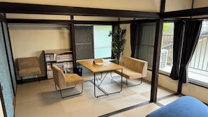 A traditional Japanese-style room with tatami flooring, a low table, two cushioned chairs, a bookshelf, and a large window with curtains. - JapaneseTraditional house ONDa (Zushi)