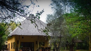 Edificio con techo de paja, un porche y zona de estar al aire libre, rodeado de un jardín ajardinado.
