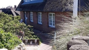 A traditional thatched-roof house with a brick facade, a stone pathway, and a wooden fence. - Haus Ruusenhoog - Apartment 7 (Sylt)