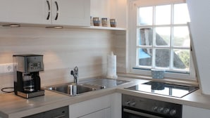 A modern kitchen with white cabinets, a coffee maker, a sink, and an oven. - Haus Ruusenhoog - Apartment 7 (Sylt)