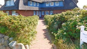 A traditional house with a steeply pitched thatched roof, a brick lower section, and a pathway leading to the entrance. - Haus Ruusenhoog - Apartment 7 (Sylt)