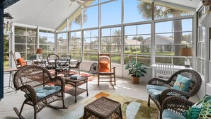 A sunroom with wicker furniture, a ceiling fan, and large windows offering a view of the neighborhood. - Sea Colony Monthly Retreat | Canal View | Steps to Private Beach & Pool | Dog Friendly (Palm Coast)