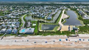 An aerial view of a coastal residential area with multiple houses, a large swimming pool, and a beach with umbrellas. - Sea Colony Monthly Retreat | Canal View | Steps to Private Beach & Pool | Dog Friendly (Palm Coast)