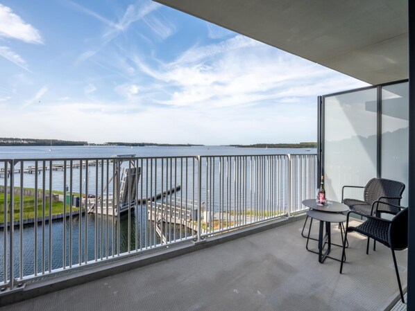 A balcony with a view of a body of water, a dock, and a small table with chairs.