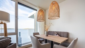 Spiseområde i moderne stil med et træbord, grå polstrede stole og havudsigt gennem store vinduer.