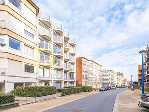 A multi-story residential building with balconies, a paved street, and parked cars. - Apartment by Belgian Sea and Dunes (Koksijde)