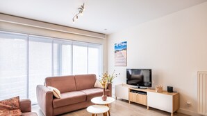 Ein modernes Wohnzimmer mit einem braunen Sofa, einem kleinen runden Tisch und einem Fernseher auf einem Holzschrank.