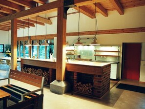 A kitchen with a brick island, wooden beams, pendant lighting, and a view through large windows. - Lubeck Comfortable Holiday Residence (Pronstorf)