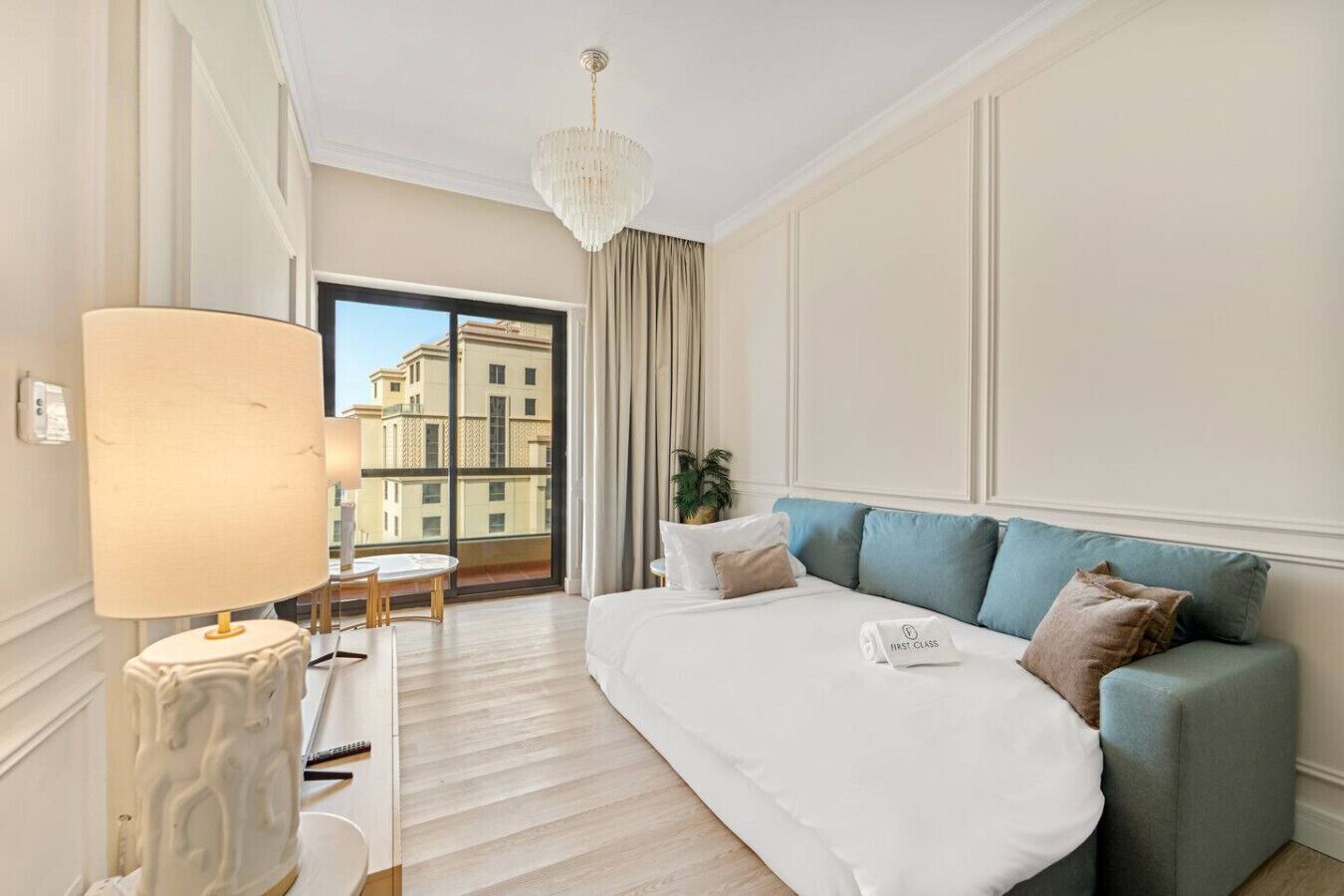 Ein Hotelzimmer mit einem großen Bett, einer Couch, einem Schreibtisch mit Lampe und Blick auf Gebäude durch ein großes Fenster.