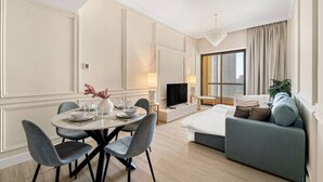 A modern hotel room with a dining area, a sofa, a TV, and a large window with curtains. - World Class | 1BR | Breathtaking Beach Views (JBR, Dubai)