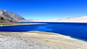 Een uitgestrekt, helderblauw meer omgeven door bergen onder een heldere lucht.